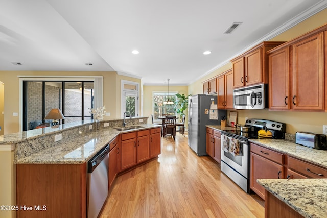 kitchen with stainless steel appliances, a sink, light wood-style floors, brown cabinetry, and a large island with sink