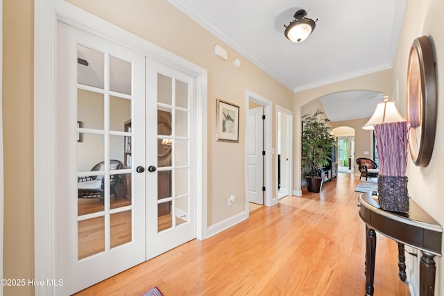 hallway featuring arched walkways, french doors, crown molding, light wood finished floors, and baseboards