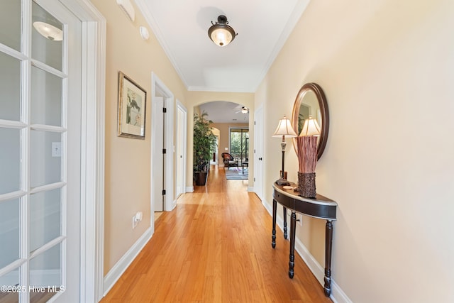 hall featuring light wood finished floors, baseboards, arched walkways, and ornamental molding