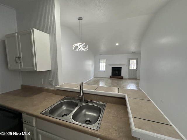 kitchen with a fireplace with raised hearth, a sink, white cabinets, vaulted ceiling, and dishwasher