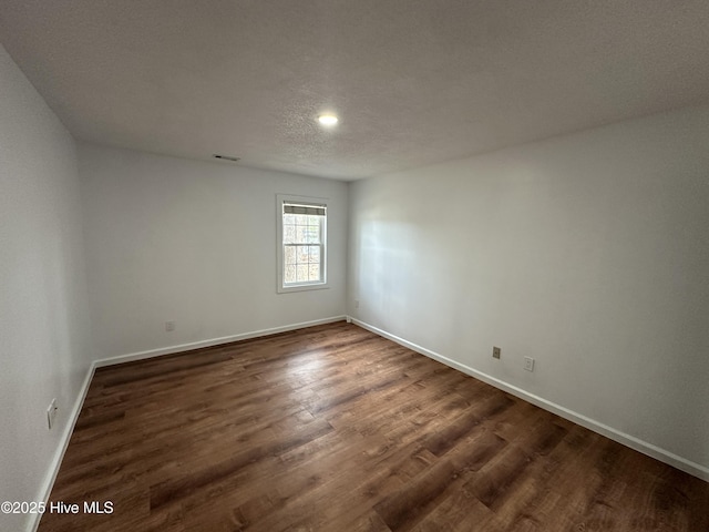 empty room with dark wood-style floors, visible vents, a textured ceiling, and baseboards