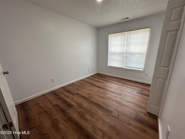 empty room featuring dark wood-style floors, a textured ceiling, visible vents, and baseboards