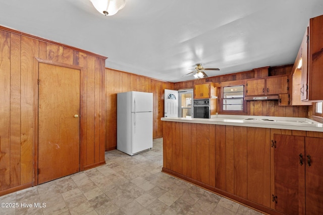 kitchen featuring cooktop, light countertops, brown cabinetry, freestanding refrigerator, and black oven