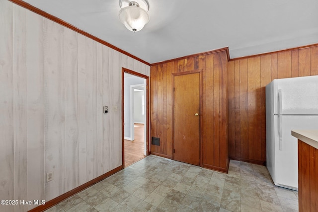 interior space with wooden walls, visible vents, ornamental molding, freestanding refrigerator, and brown cabinets