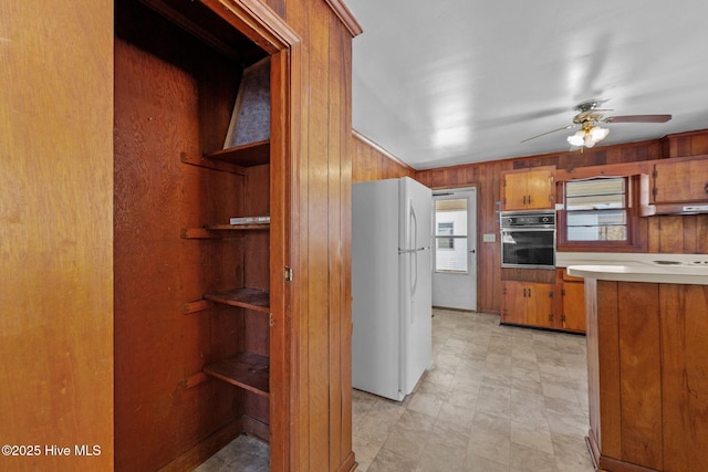 kitchen featuring oven, under cabinet range hood, light countertops, freestanding refrigerator, and brown cabinets