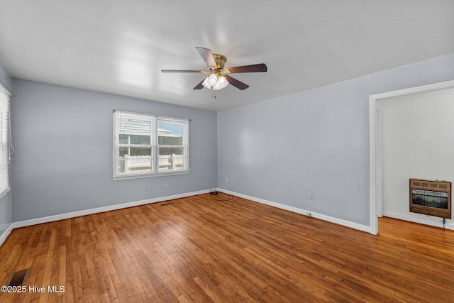 spare room featuring ceiling fan, visible vents, baseboards, heating unit, and hardwood / wood-style floors