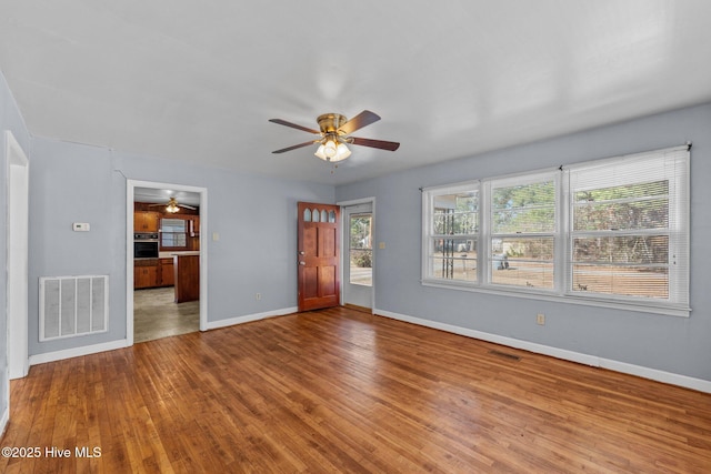 unfurnished living room with a ceiling fan, visible vents, baseboards, and wood finished floors