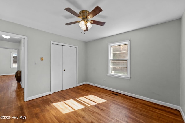 unfurnished bedroom with a closet, multiple windows, baseboards, and wood finished floors