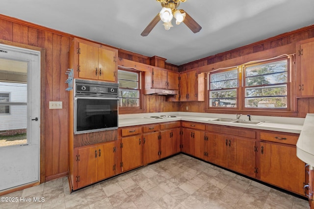 kitchen featuring a wealth of natural light, light countertops, a sink, oven, and under cabinet range hood