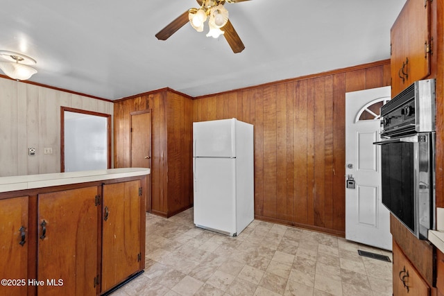 kitchen with wood walls, brown cabinetry, oven, and freestanding refrigerator