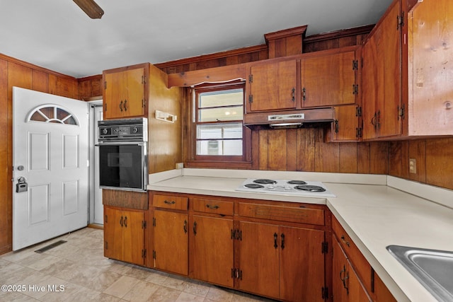 kitchen featuring brown cabinetry, white electric stovetop, black oven, and under cabinet range hood