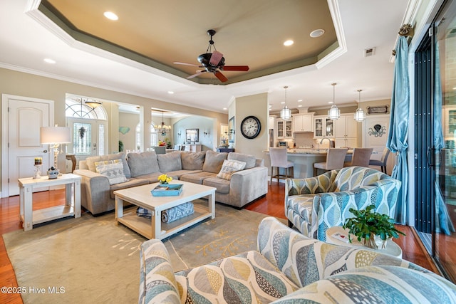 living area featuring visible vents, ceiling fan with notable chandelier, a tray ceiling, wood finished floors, and crown molding