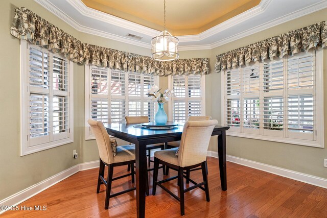 dining area featuring visible vents, light wood-style flooring, arched walkways, ornamental molding, and a raised ceiling