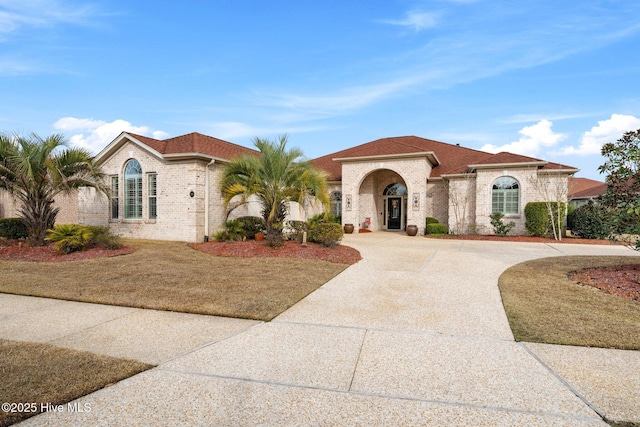 mediterranean / spanish house with curved driveway, brick siding, and a shingled roof