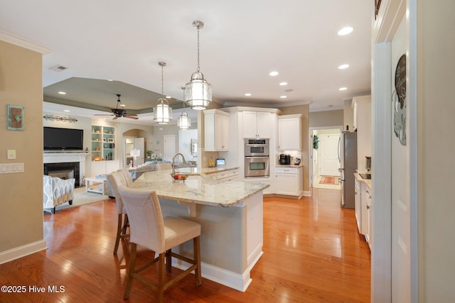 kitchen featuring a kitchen bar, light wood-style flooring, a fireplace, stainless steel appliances, and a sink