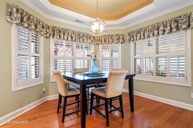 dining room featuring visible vents, ornamental molding, a tray ceiling, wood finished floors, and baseboards