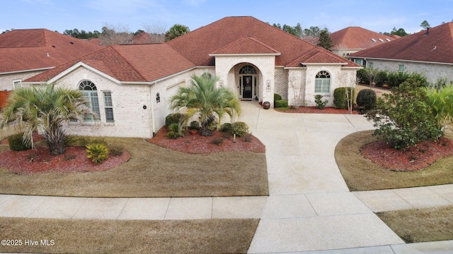 mediterranean / spanish-style home with brick siding, driveway, and a shingled roof