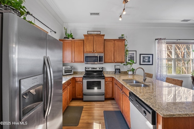 kitchen with appliances with stainless steel finishes, brown cabinets, a peninsula, crown molding, and a sink