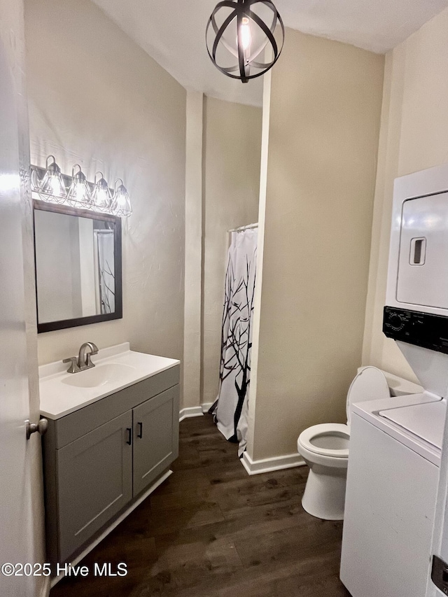 bathroom with toilet, wood finished floors, vanity, baseboards, and stacked washing maching and dryer