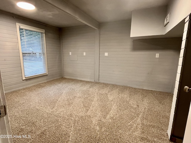 carpeted spare room with beamed ceiling and wooden walls