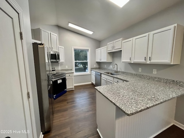 kitchen featuring lofted ceiling, a peninsula, dark wood-type flooring, a sink, and appliances with stainless steel finishes