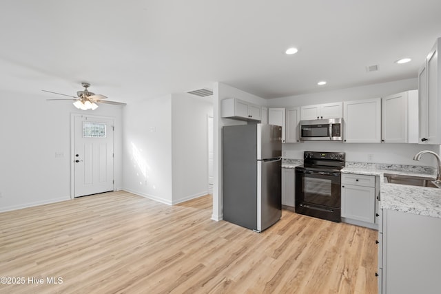 kitchen with stainless steel appliances, visible vents, light wood-style floors, a sink, and light stone countertops