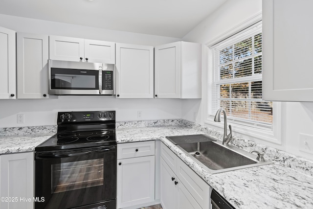 kitchen featuring electric range, white cabinets, stainless steel microwave, light stone countertops, and a sink