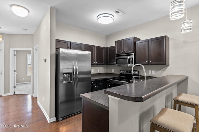 kitchen with visible vents, dark countertops, appliances with stainless steel finishes, a peninsula, and dark brown cabinets