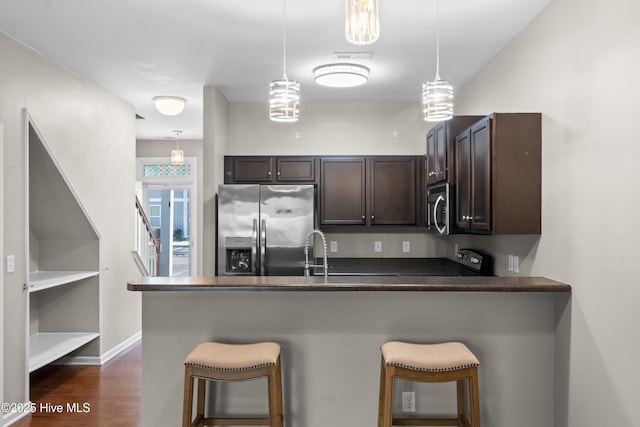 kitchen with dark brown cabinetry, stainless steel appliances, dark wood-type flooring, a peninsula, and a kitchen bar