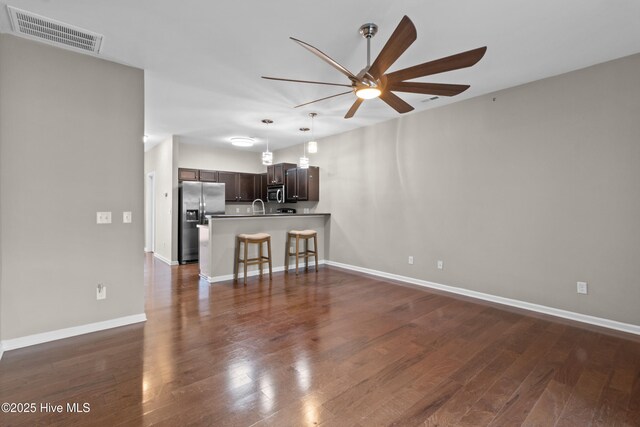 unfurnished living room with visible vents, baseboards, dark wood-style floors, ceiling fan, and a sink