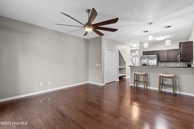 unfurnished living room featuring ceiling fan, dark wood-type flooring, and baseboards