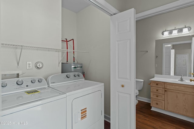 washroom with washing machine and dryer, dark wood-type flooring, a sink, baseboards, and water heater