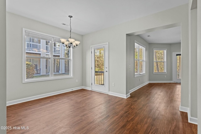 unfurnished dining area featuring a notable chandelier, baseboards, dark wood finished floors, and a wealth of natural light