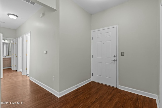 corridor with dark wood-type flooring, visible vents, and baseboards