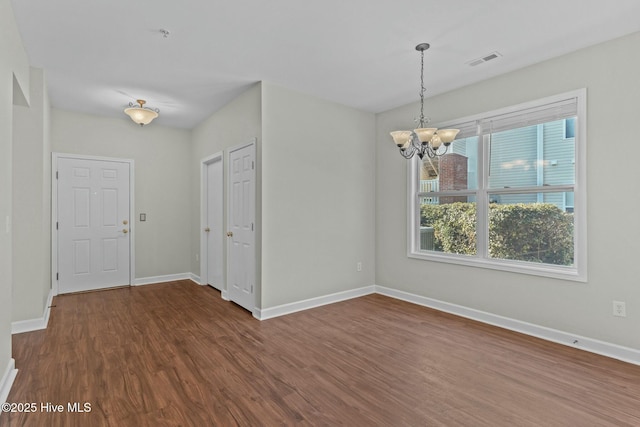 unfurnished dining area featuring dark wood-type flooring, visible vents, a notable chandelier, and baseboards