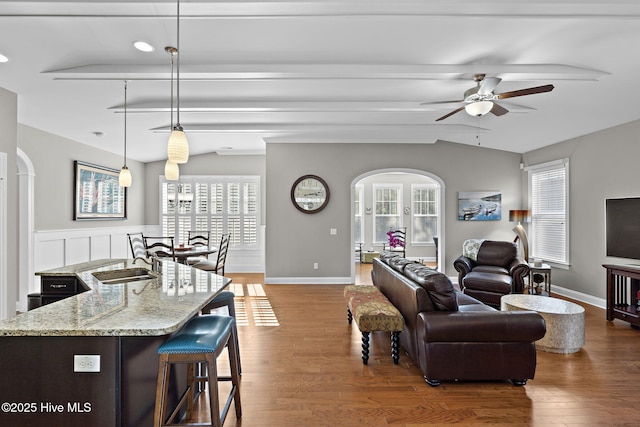 living room featuring vaulted ceiling with beams, a healthy amount of sunlight, arched walkways, and wood finished floors