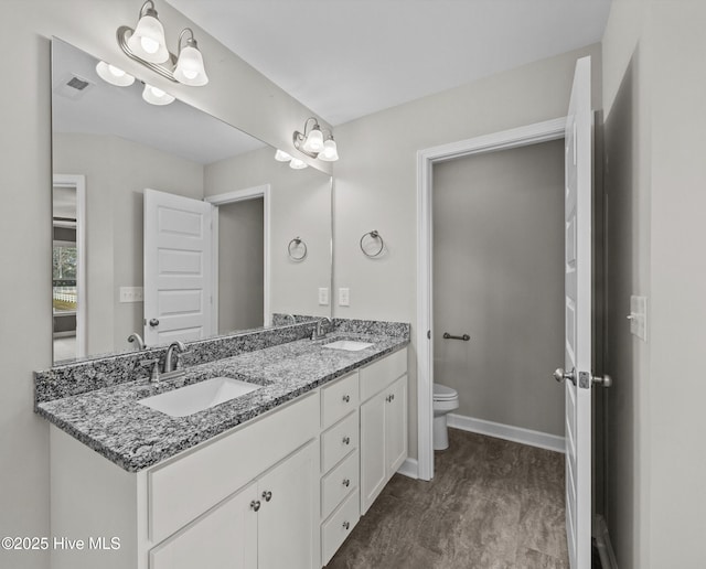 full bath with toilet, double vanity, baseboards, and a sink