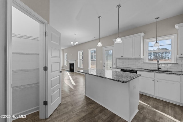 kitchen featuring a sink, a center island, tasteful backsplash, dark stone countertops, and a glass covered fireplace