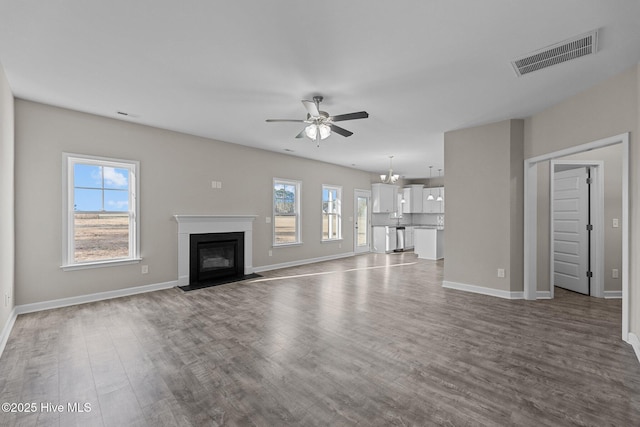 unfurnished living room with dark wood-type flooring, a fireplace with flush hearth, visible vents, and a healthy amount of sunlight