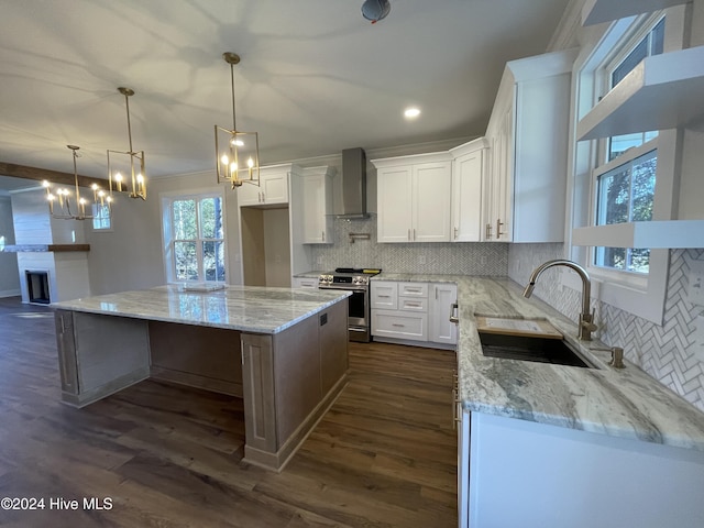 kitchen featuring stainless steel gas stove, wall chimney exhaust hood, a center island, white cabinetry, and a sink