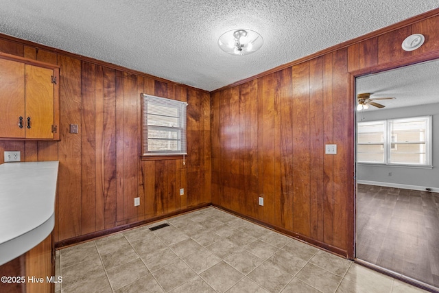 spare room with ceiling fan, wooden walls, visible vents, and a textured ceiling