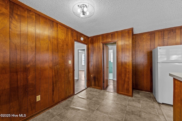 interior space with wooden walls, brown cabinets, freestanding refrigerator, a textured ceiling, and crown molding