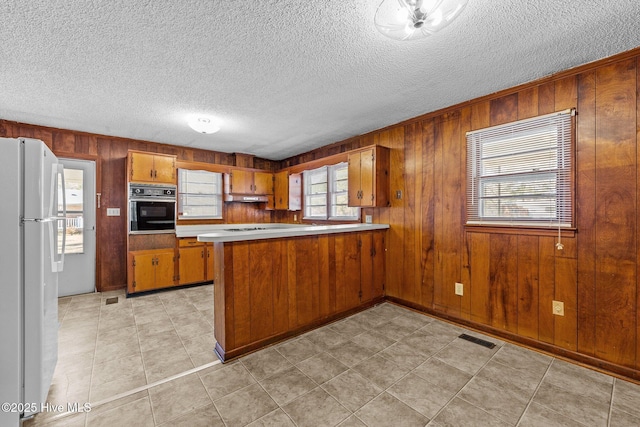 kitchen with black oven, visible vents, brown cabinetry, and freestanding refrigerator