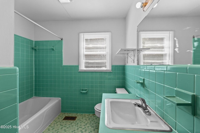 bathroom featuring tile walls, bathing tub / shower combination, visible vents, toilet, and a sink