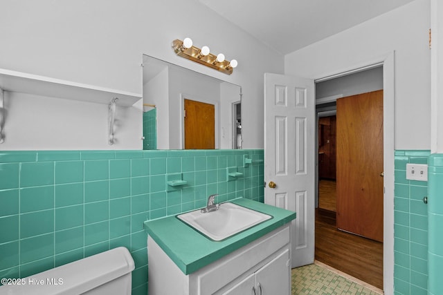 bathroom featuring toilet, a wainscoted wall, tile walls, and vanity