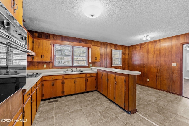 kitchen featuring a peninsula, a sink, visible vents, light countertops, and brown cabinetry