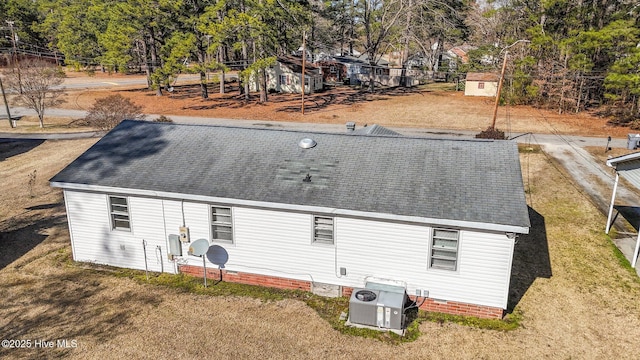 back of house featuring ac unit, roof with shingles, a lawn, and central air condition unit