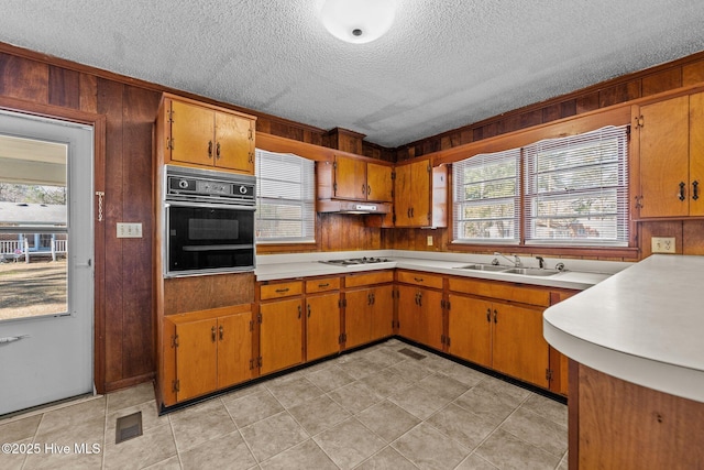 kitchen featuring white stovetop, oven, light countertops, under cabinet range hood, and a sink