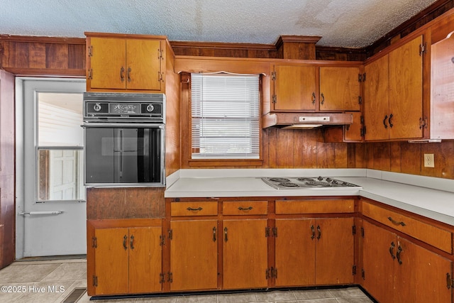 kitchen featuring oven, light countertops, a textured ceiling, under cabinet range hood, and stainless steel electric stovetop