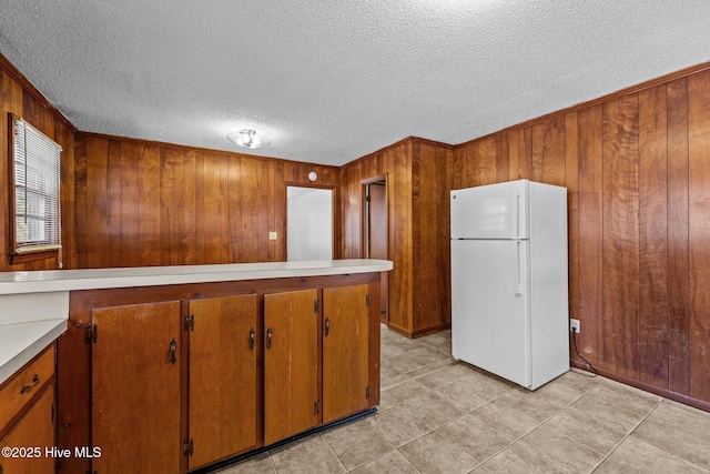 kitchen featuring light countertops, wood walls, brown cabinetry, and freestanding refrigerator